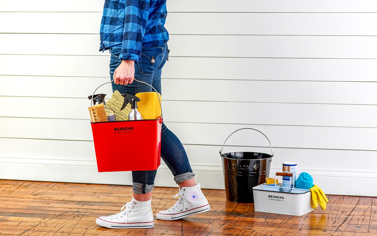 woman walking with a white pail full of cleaning products and black square pail and white pail on the floor