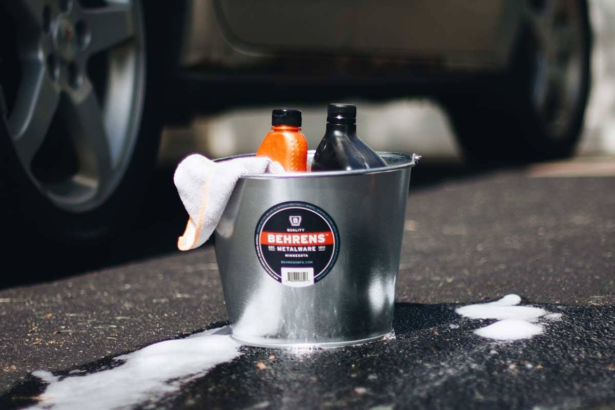 Galvanized metal pail with car cleaning supplies in it next to a car