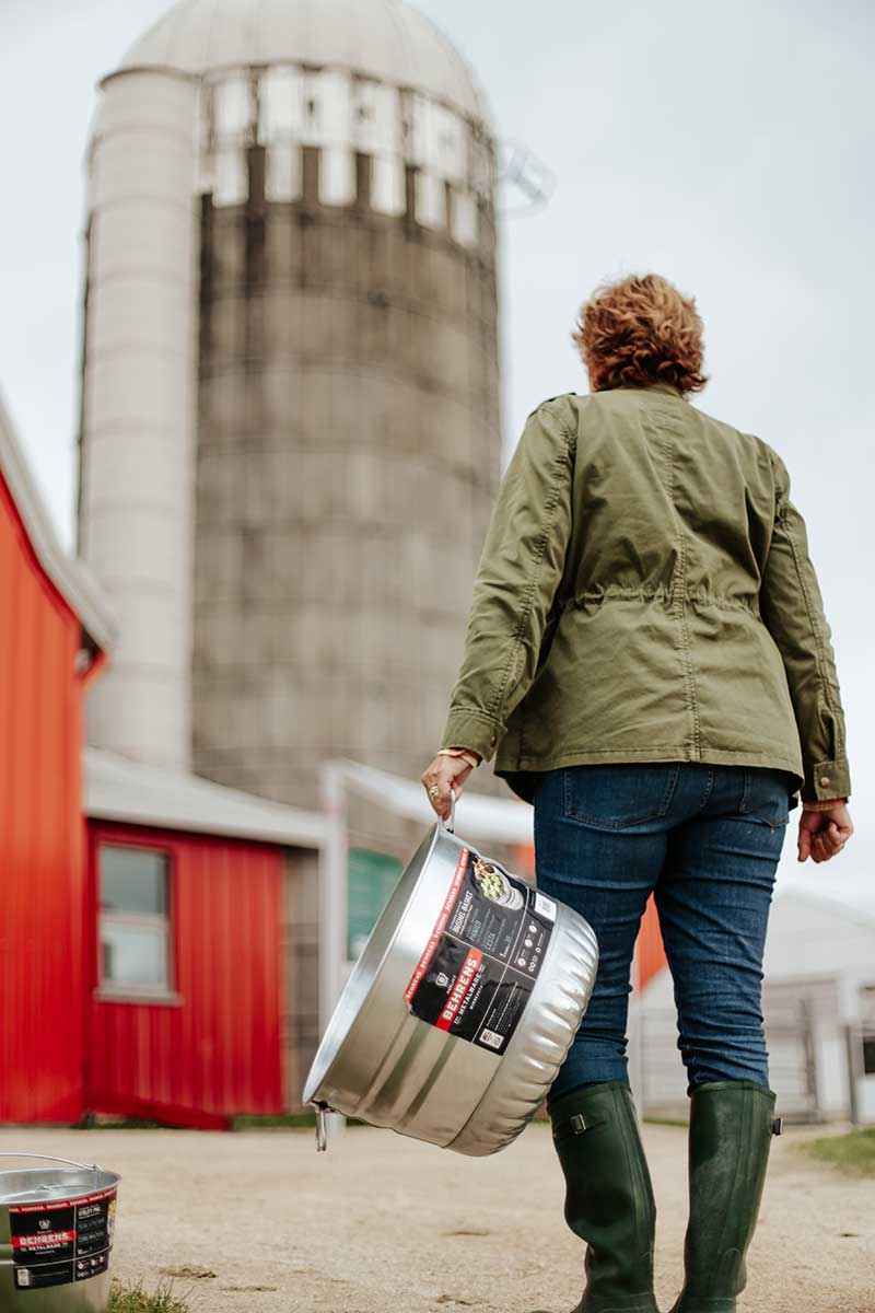 farm-bushel Woman carrying empty galvanized tub with farm in background